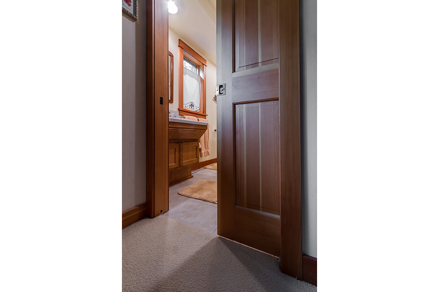 A partially open wooden pocket door separates the linoleum of the bathroom from the carpet of the adjoining room. 